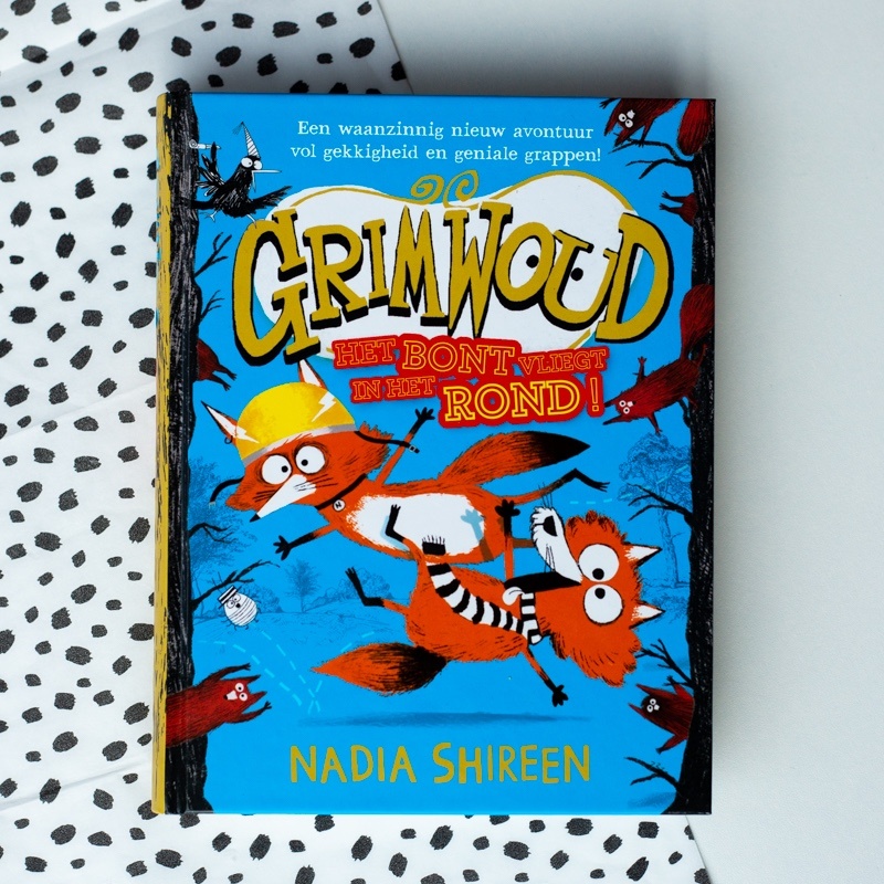 Het bont vliegt in het rond voorkant met SLV rand voorkant Grimwoud 2 Het bont vliegt in het rond 2 vossen vliegend door de lucht met aan weerszijden bomen en eekhoorns voorkant cover omslag kaft