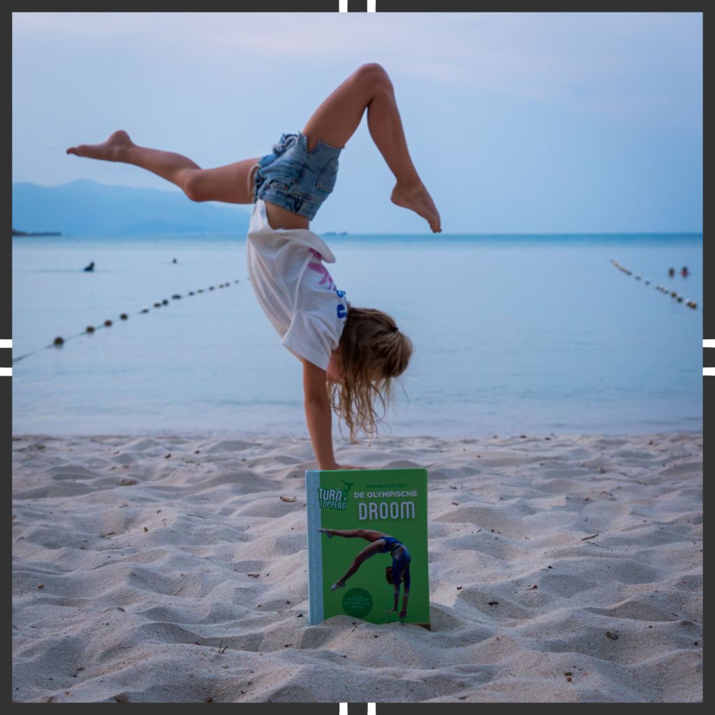 De olympische droom met SLV kader en kind dat handstand doet bovenop het boek aan het strand